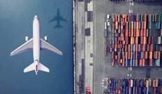 Flygplan flyger över en hamn full med containrar